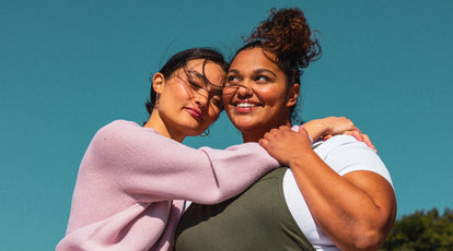 woman in pink sweater and woman in green overalls hug