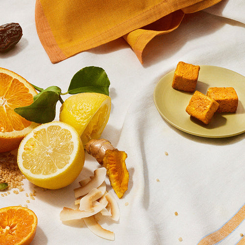 Three GEM Citrus Ginger Daily Essentials nutrient-dense multivitamin Bites on a plate featured on a table with oranges, lemons, and linens.